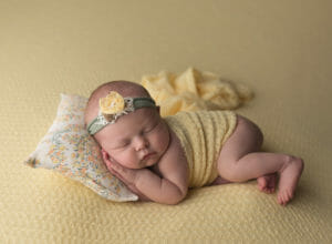 baby girl in yellow with floral pillow side laying pose in New Orleans