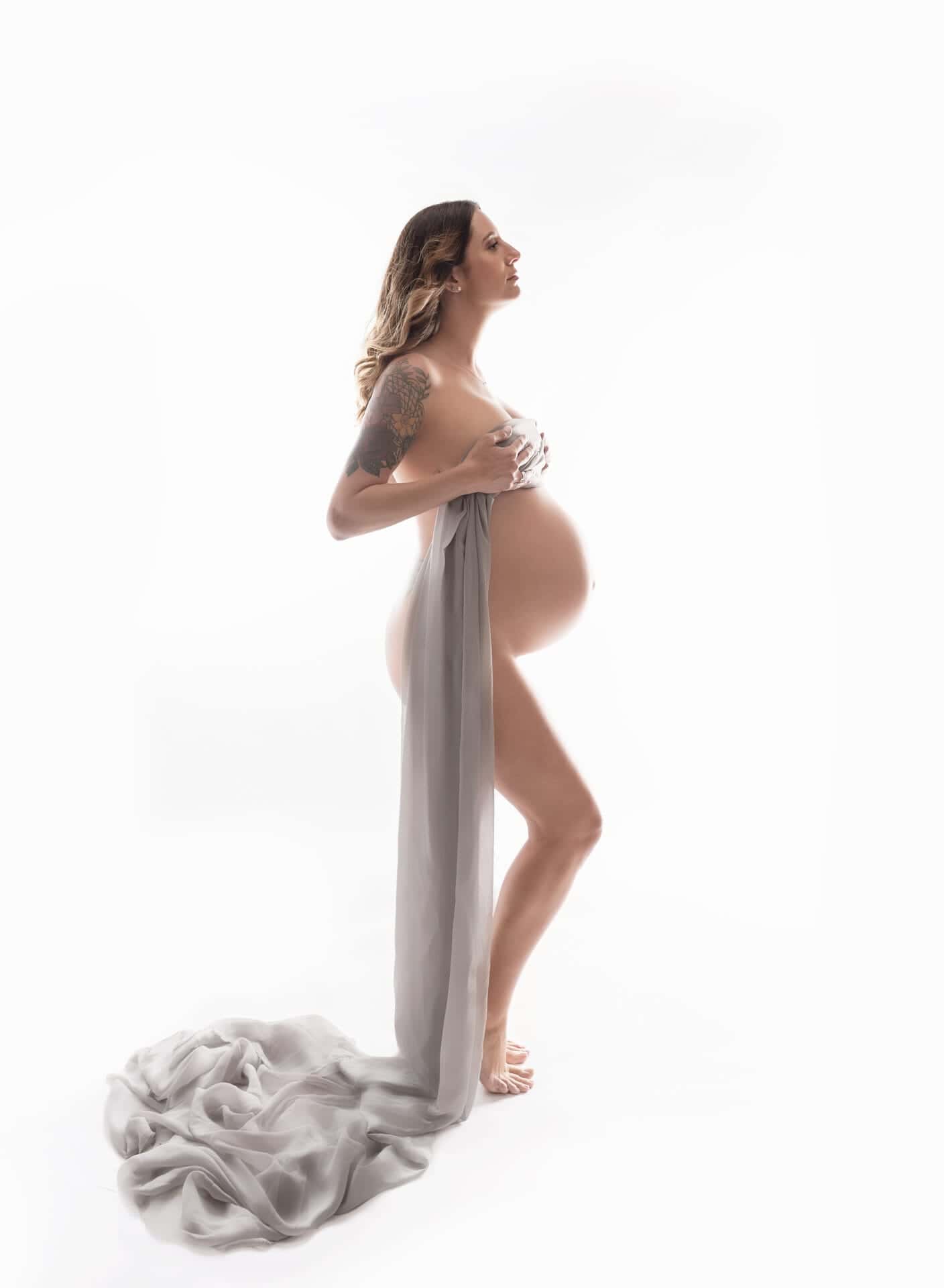 A pregnant mom in the studio with fabric draped around her body and her pregnant belly exposed.