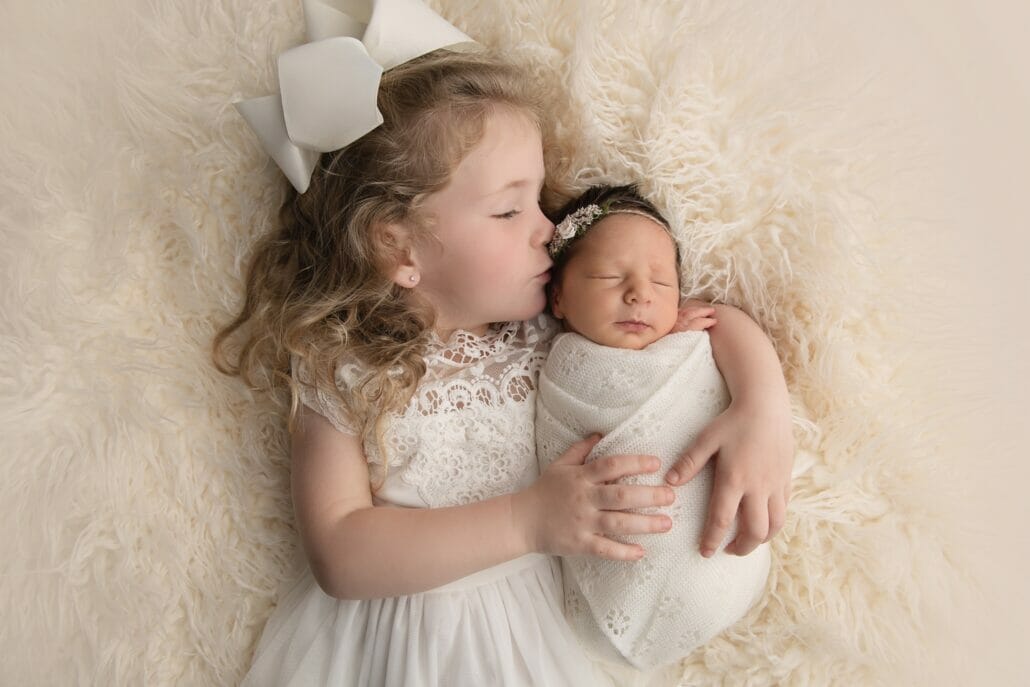 A sibling lays beside a newborn baby on a white rug for Baton Rouge newborn photography.