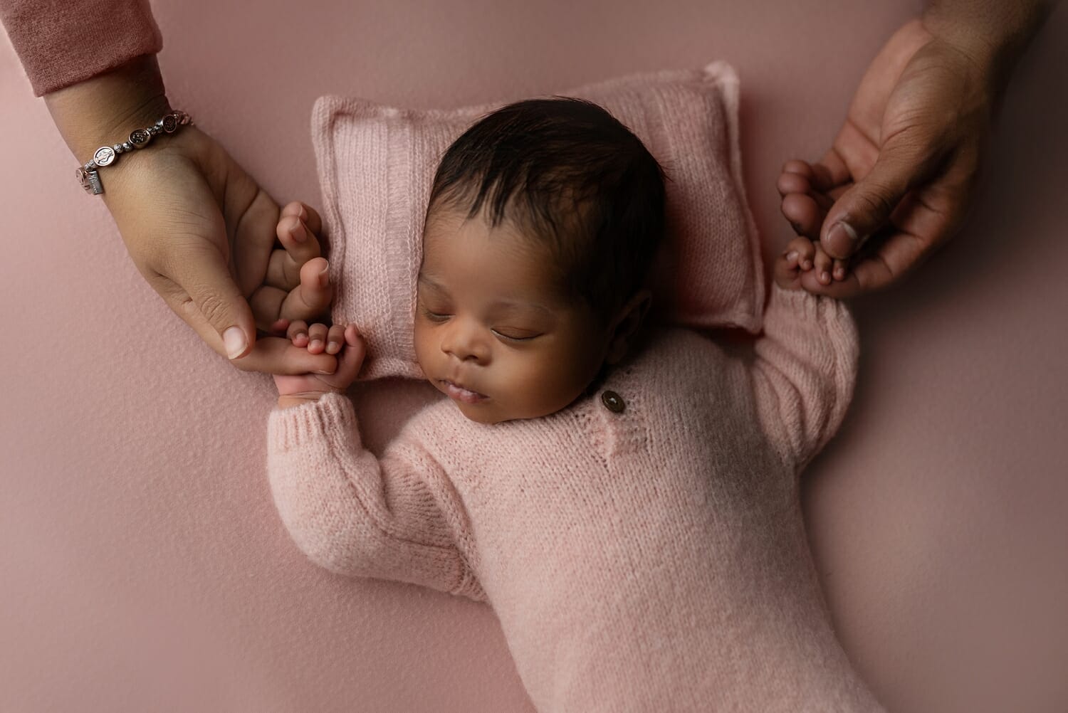 Parents hold a newborn baby's hands in a newborn photo shoot.