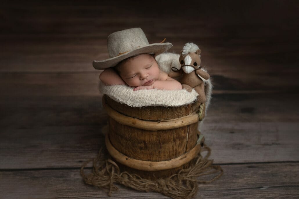 A baby wears a hat while sitting in a basket for newborn photos.