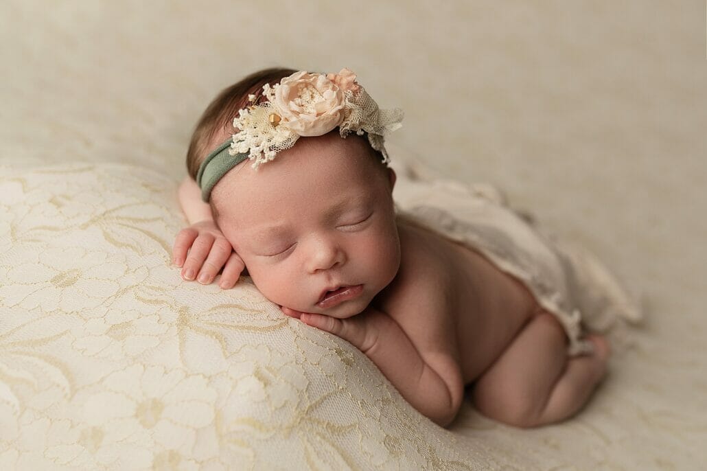 A newborn on a white backdrop wears a floral headband.