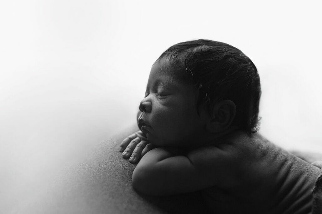 A newborn baby is silhouetted against a white back drop.