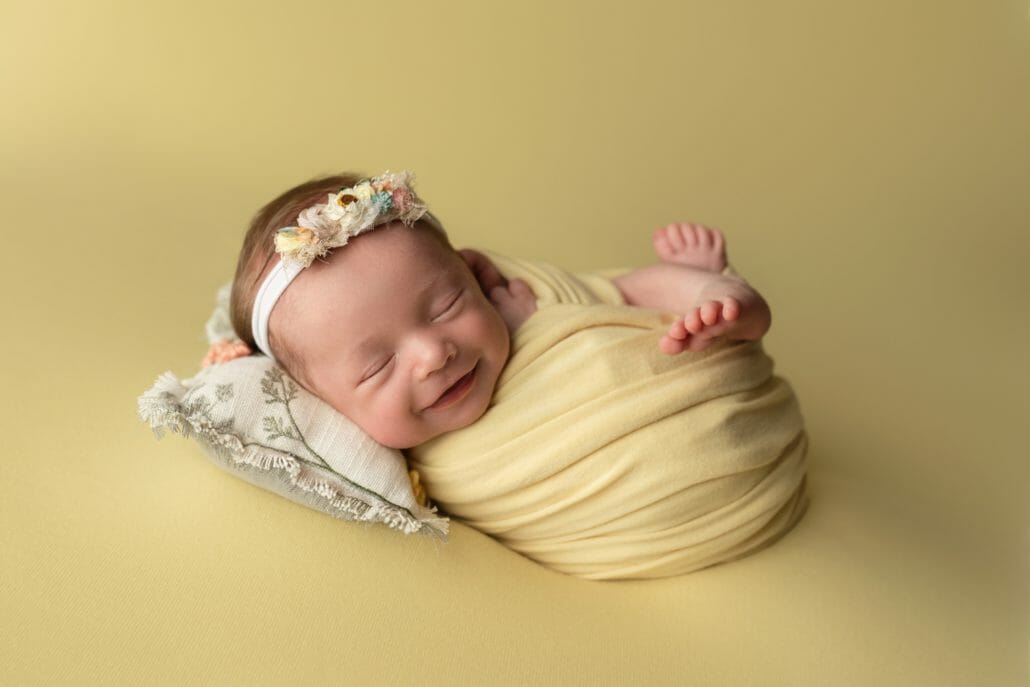 A newborn wrapped in a yellow swaddle lays on a floral pillow.