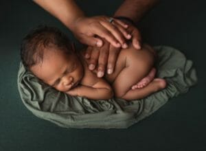 Two parents place their hands on their newborn baby's back in studio phot.