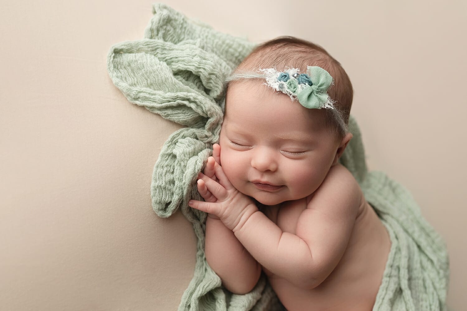 A baby with a floral headband lays on a green blanket for New Orleans newborn photography.