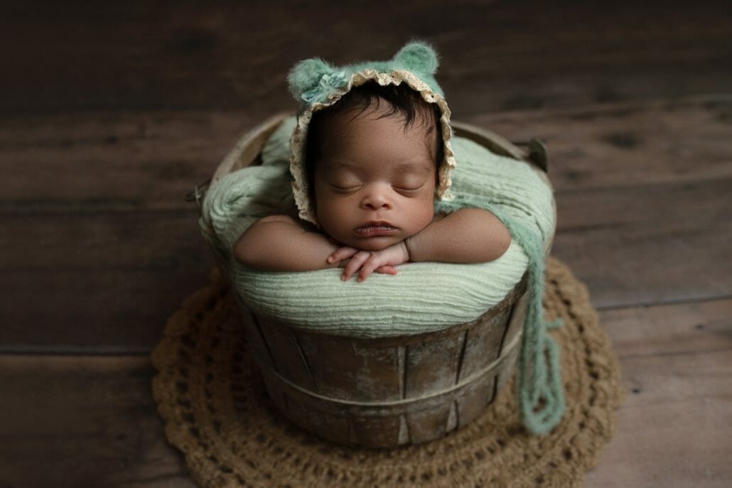 A newborn baby sleeps posed in a basket.