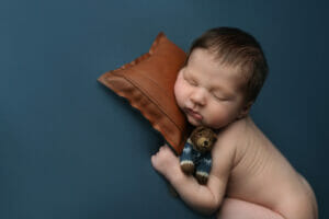 A 17 day old baby boy snuggling teddy bear on blue backdrop at Baton Rouge LA photography studio. 