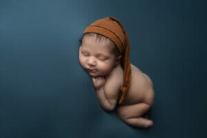 A Lafayette LA photography studio with a newborn baby boy with rust color sleepy hat on blue backdrop. 