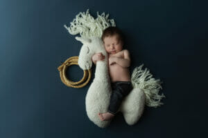 A newborn baby boy with jeans on a blue back drop on a horse at a New Orleans LA photo studio. 