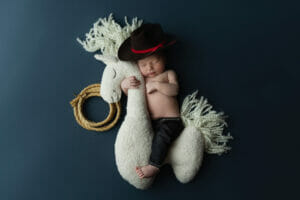 A newborn baby boy with a cowboy hat on a plush horse at Lafayette LA photo studio. 