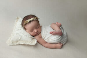 curled newborn pose, flower headband, cream neutral color