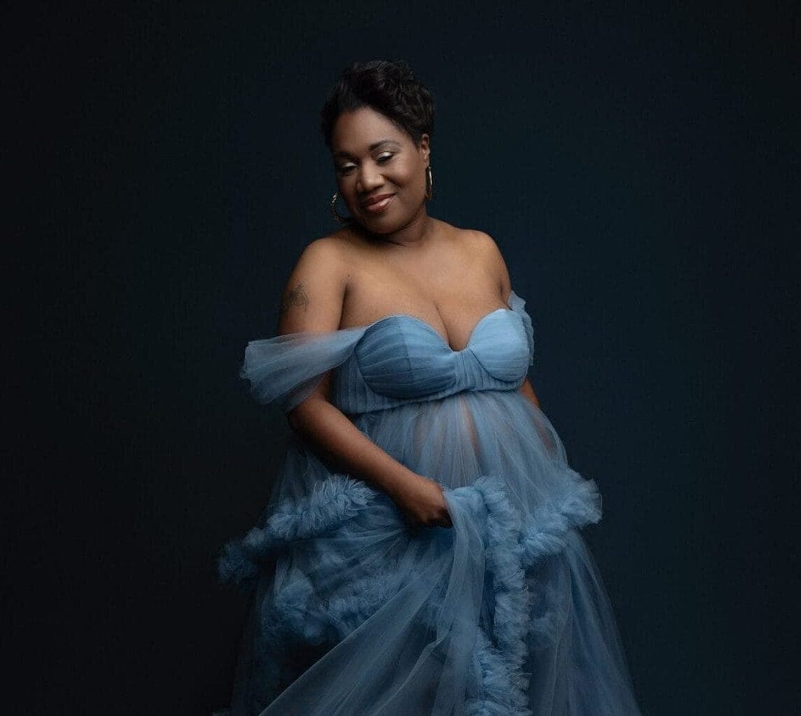 An expectant mom in the studio wearing a blue flowing gown.