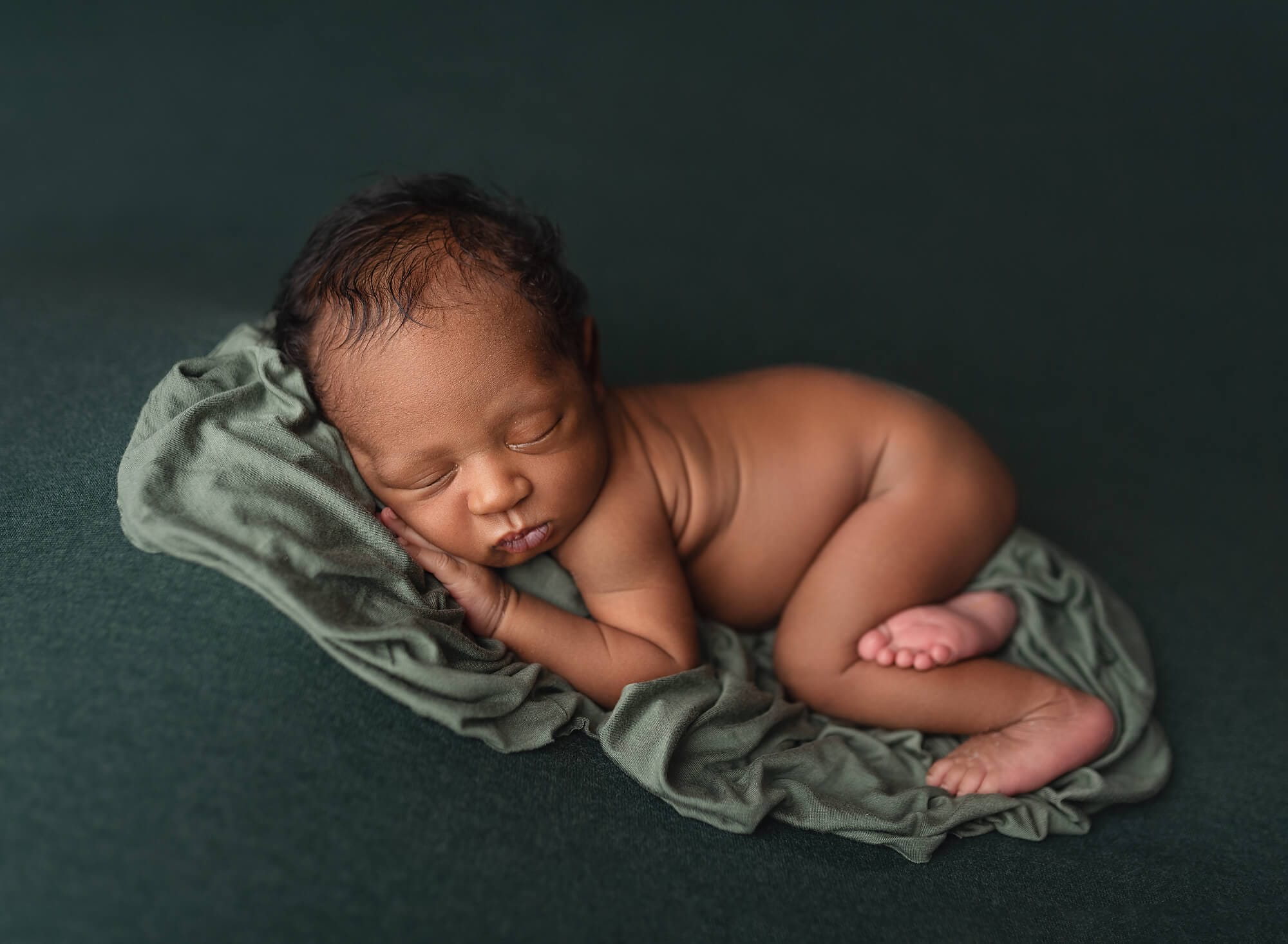 Baby boy on green backdrop lying on stomach with top Lafayette ultrasound location.