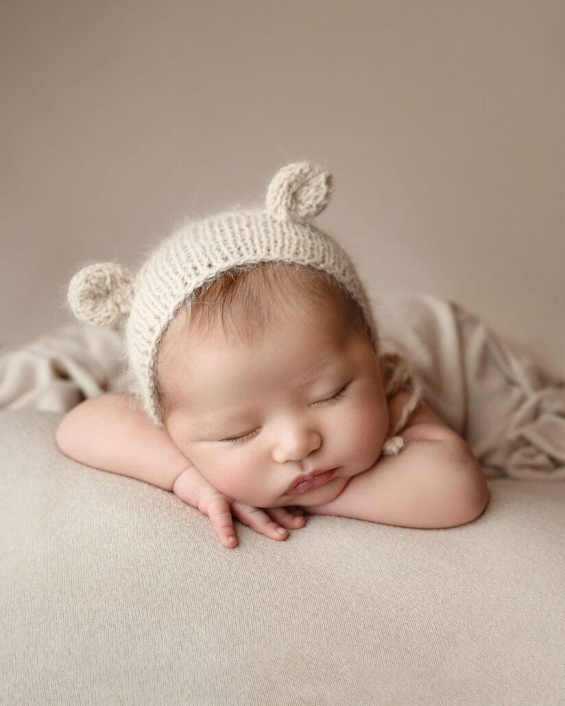 Boy boy with bear bonnet lying on tan backdrop.