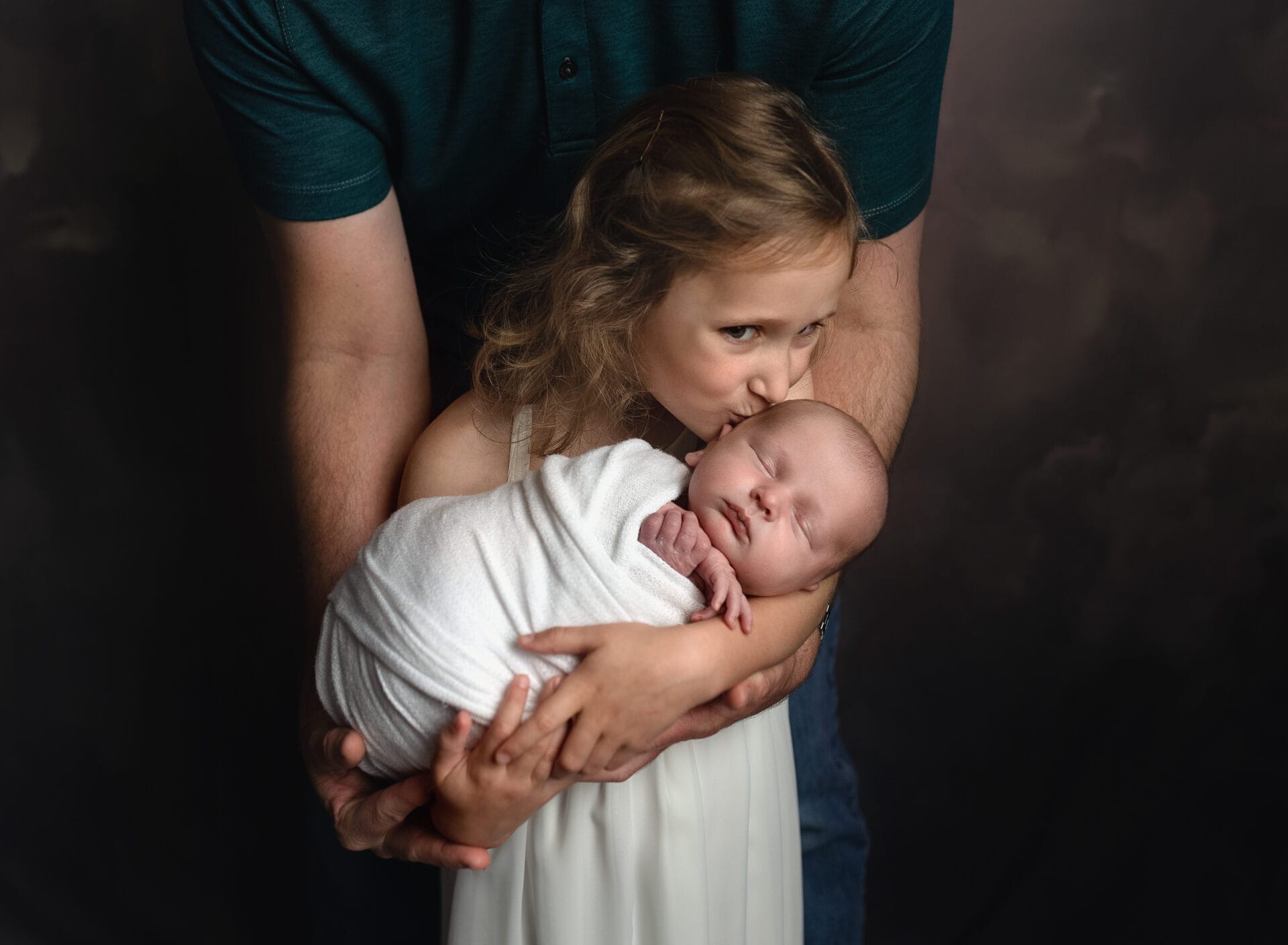 A big sister in the studio holds her baby brother with the help of her dad at Baton Rouge's top-notch daycare.