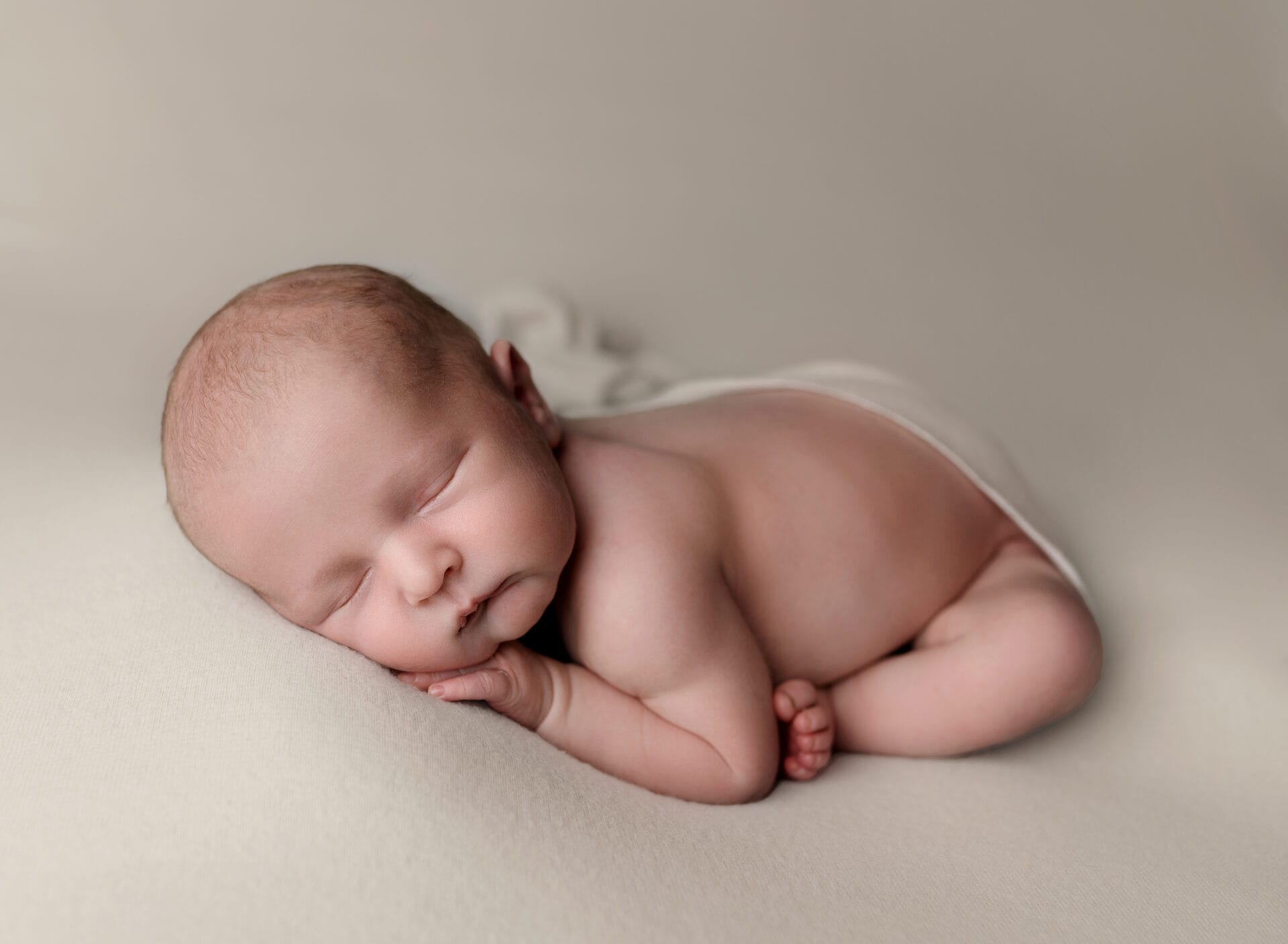 A baby boy on a cream backdrop in a taco pose at Baton Rouge's top daycare.