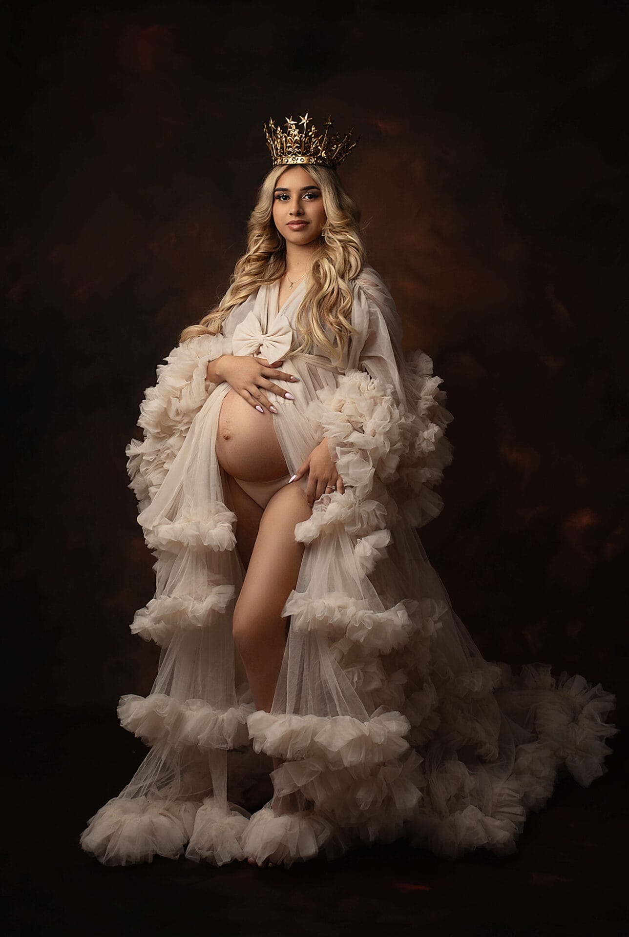 An expecting mom in the studio with a crown on her head dressed in a fluffy robe embracing her pregnant belly with Baton Rouge water birth.