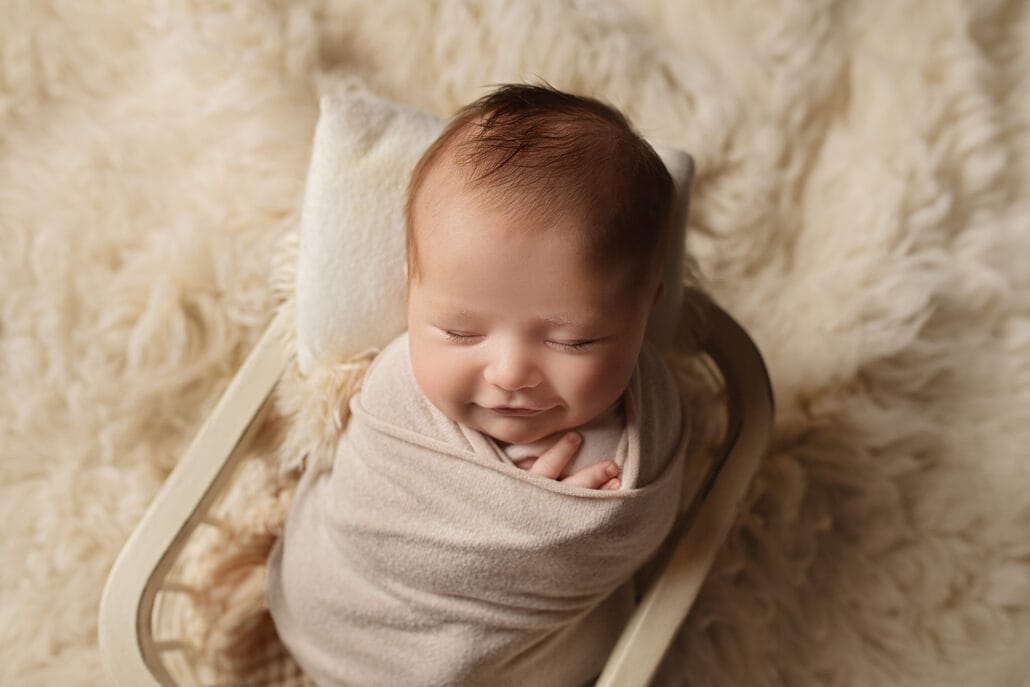 The newborn baby boy smiles and swaddles in the basket with the top New Orleans OBGYN doctor.