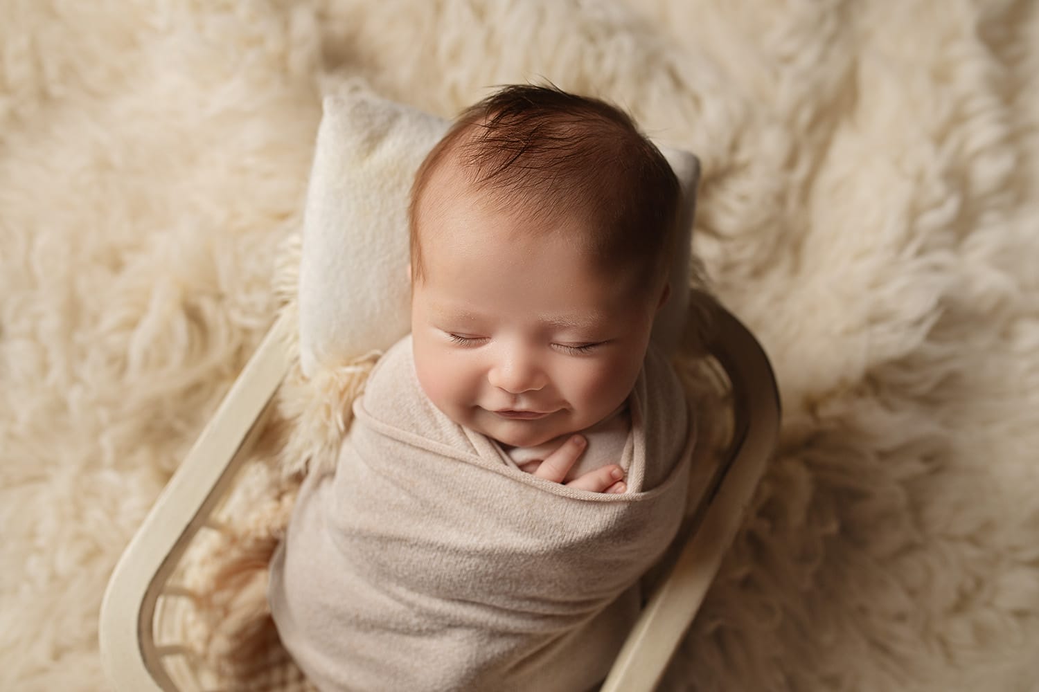 The newborn baby boy smiles and swaddles in the basket with the top New Orleans OBGYN doctor.