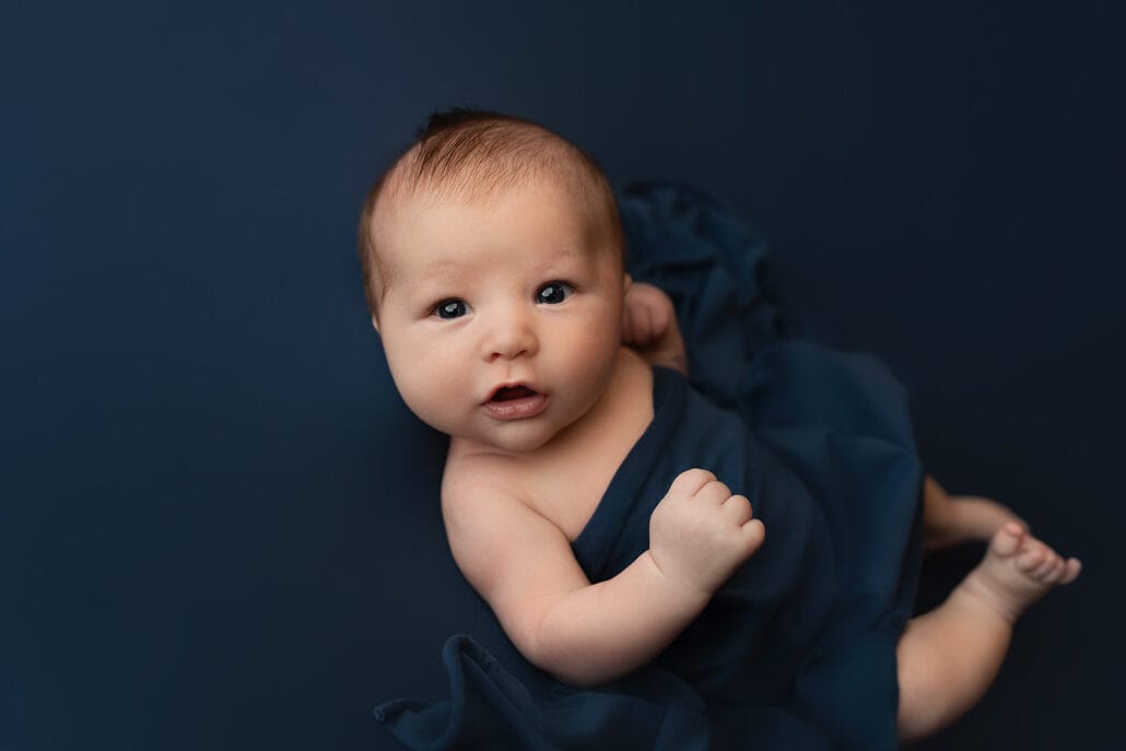 The newborn baby boy is in the studio on a navy backdrop, looking at the camera with the New Orleans OBGYN doctor.
