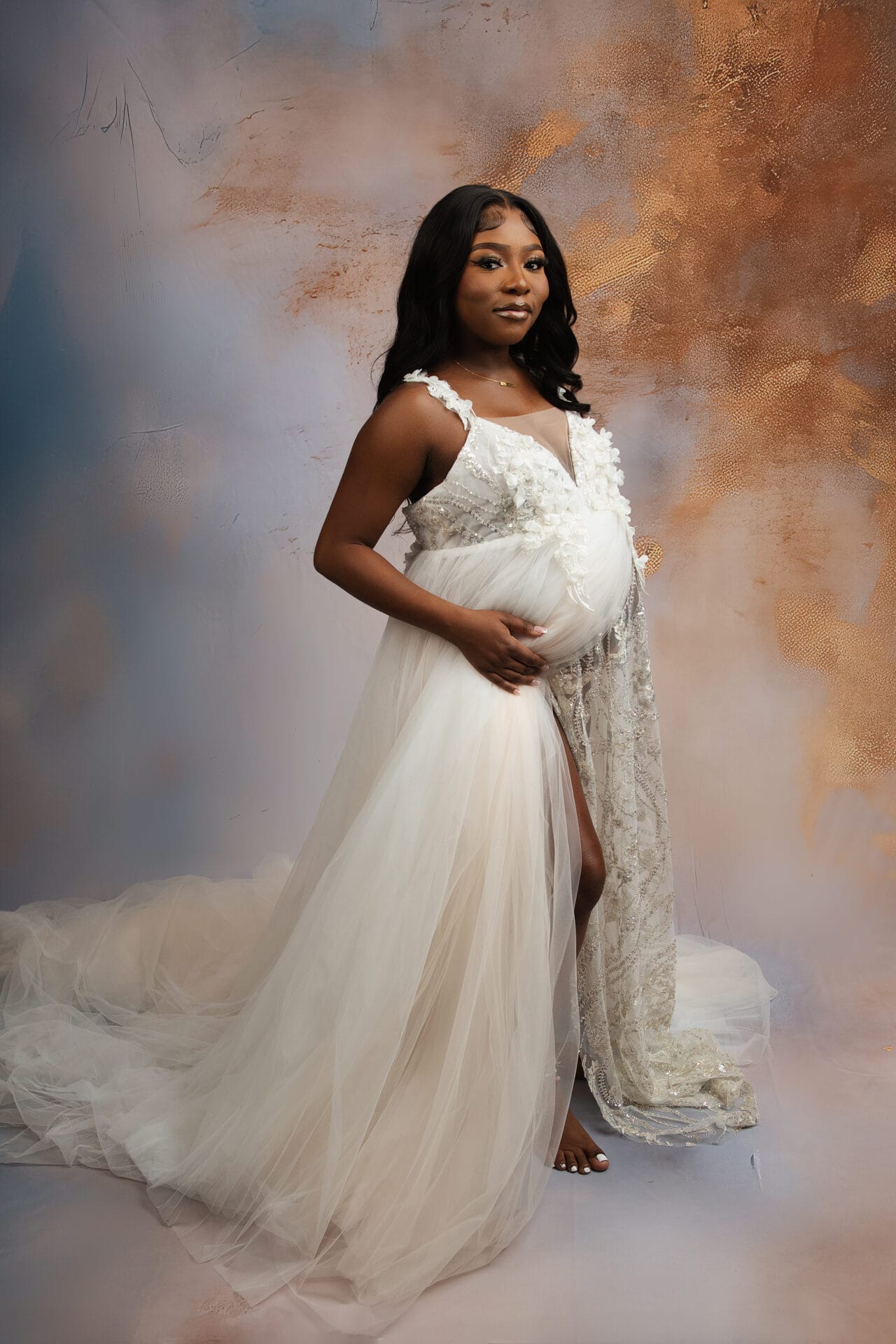 A pregnant mom with a white elegant gown embracing her pregnant belly in the studio.