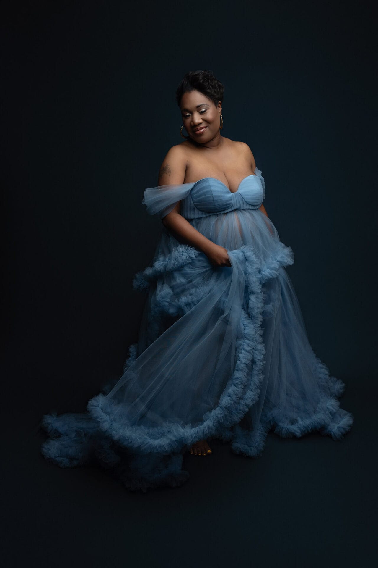 A happy mom to be dances in a studio in a blue tule maternity gown after visiting new orleans baby shower venues