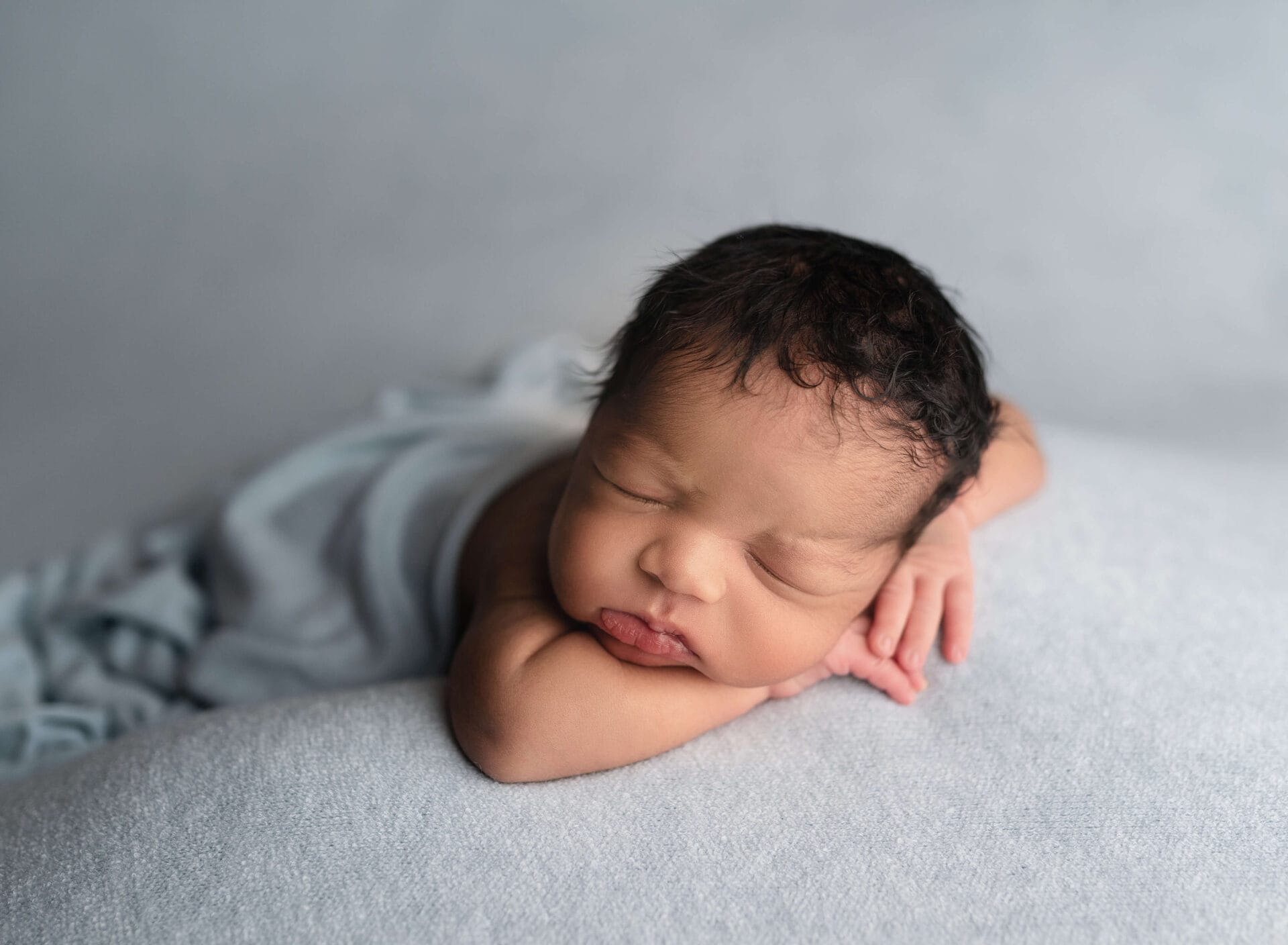 A newborn baby lays wrapped in a blue blanket with Baton Rouge newborn photographer.