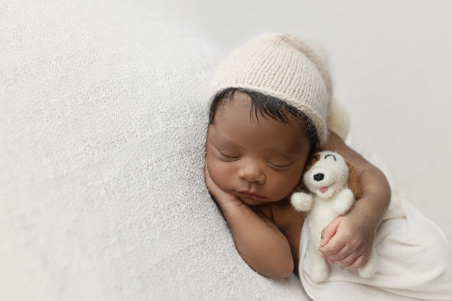 A baby is posed in a white blanket and cap holding a stuffy for Baton Rouge newborn photography.