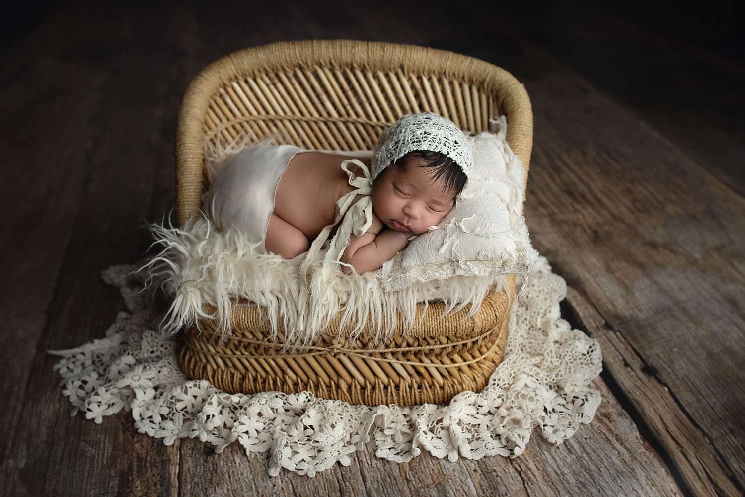 A newborn baby girl in the studio posed on her tummy on a bed with lace fabric layers.